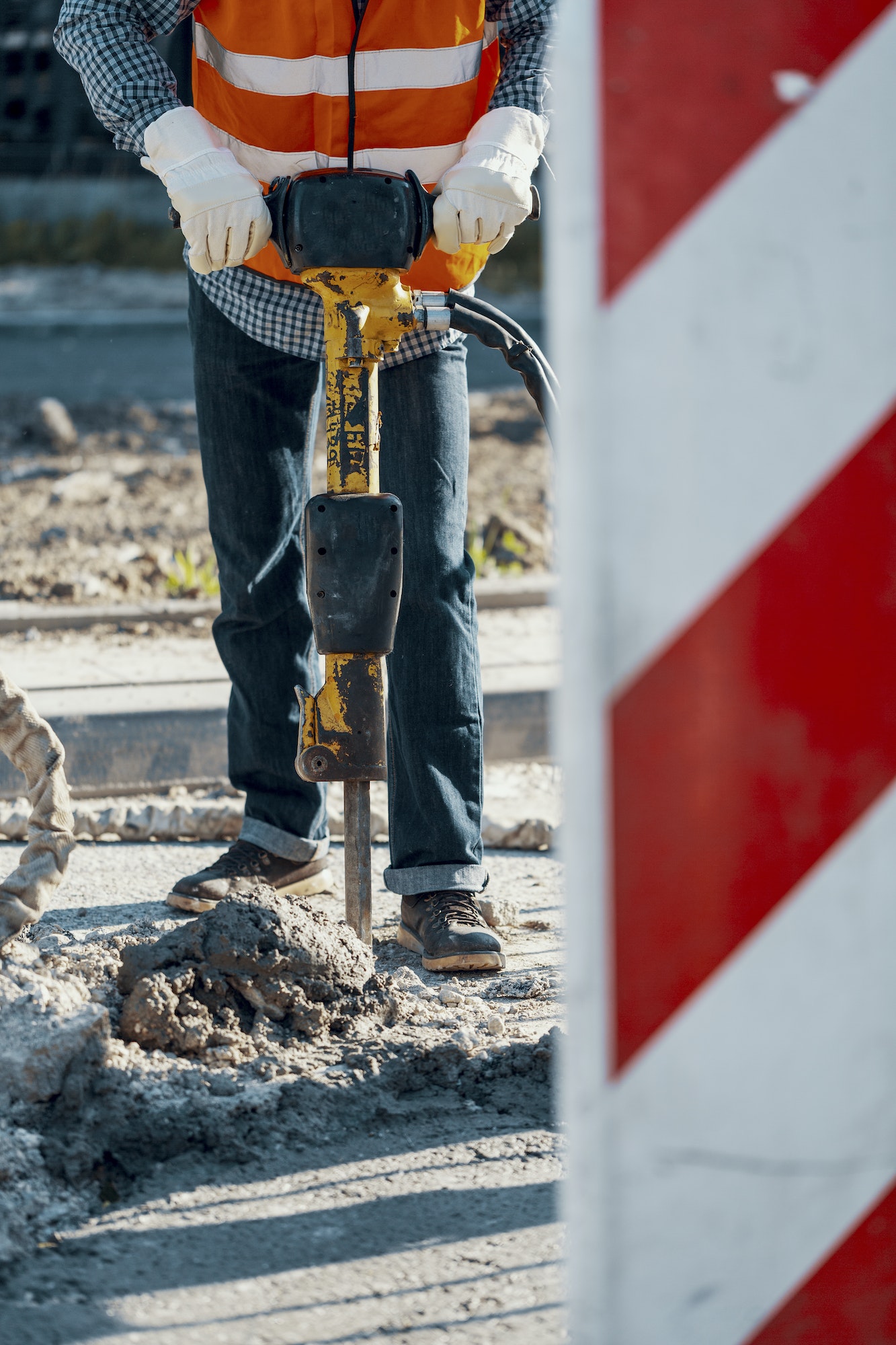 Worker in reflective vest and with drill repairing asphalt durin